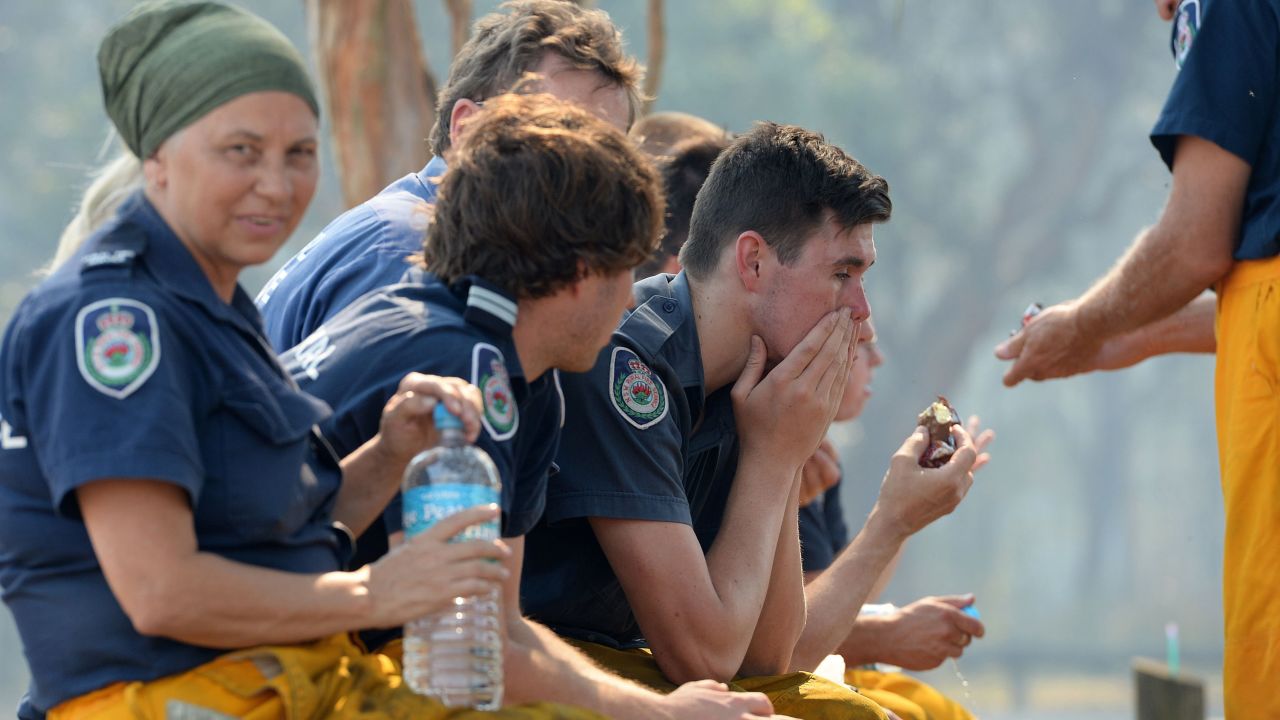 Firefighters rest as they wait for the fire front to jump a freeway in Newcastle, Australia, on October 23.