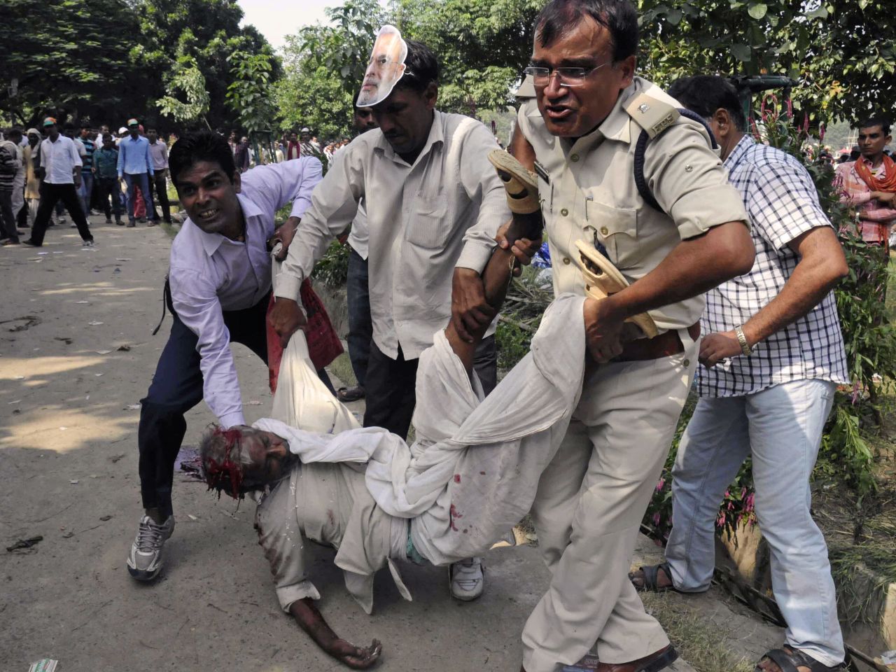 An Indian police officer and bystanders help an injured man when a series of bombs went off before a political rally.