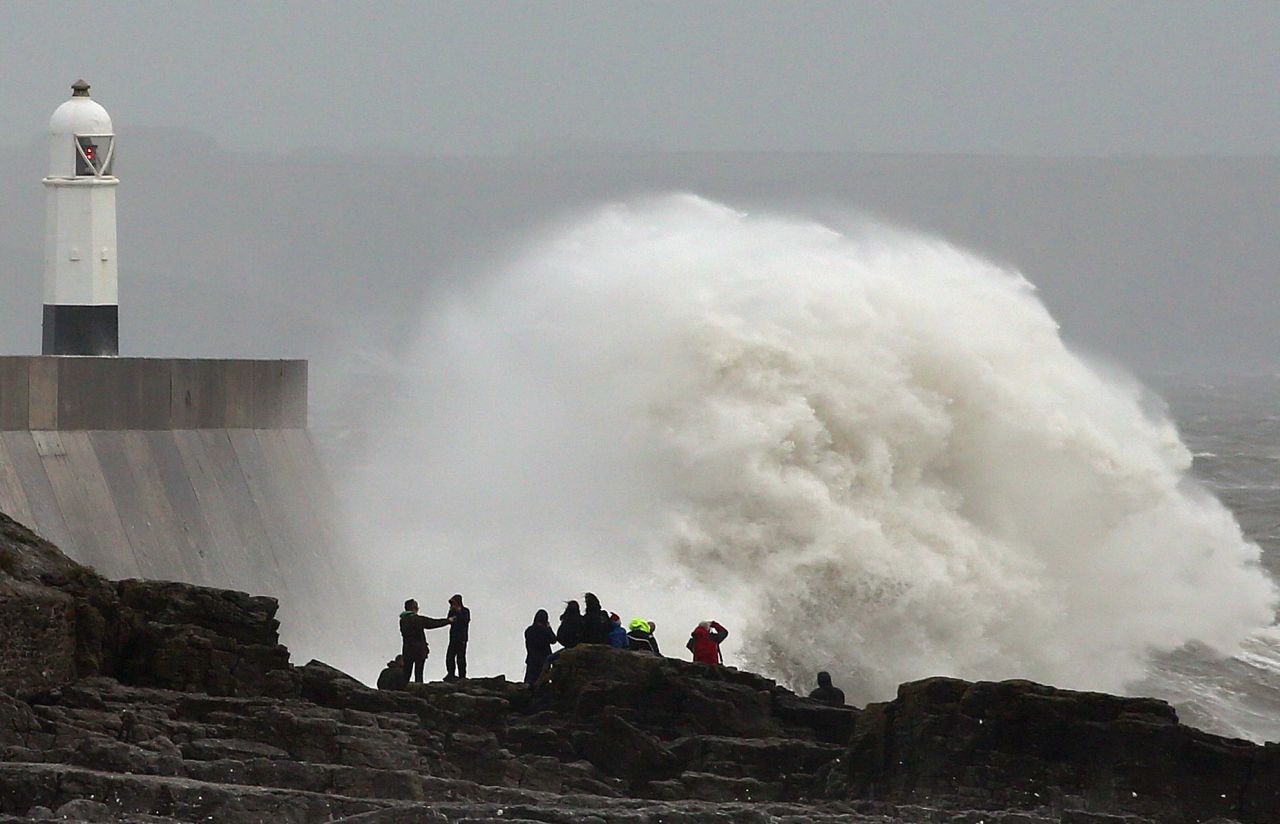 La gente se para en las rocas mientras las olas rompen contra el puerto en Porthcawl, Gales, el domingo.