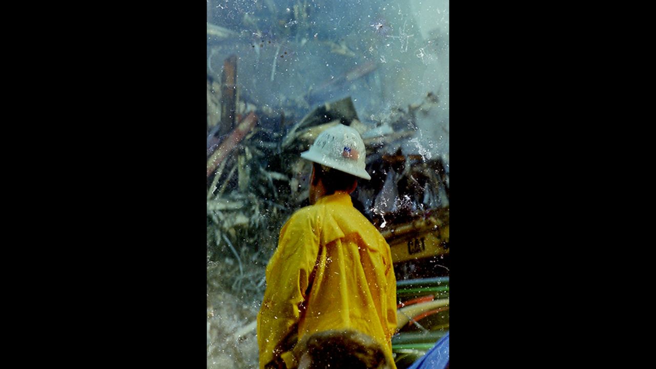 A firefighter stands before the World Trade Center rubble at ground zero. The image has scratches and water damage that give it a smoky, three-dimensional feel.