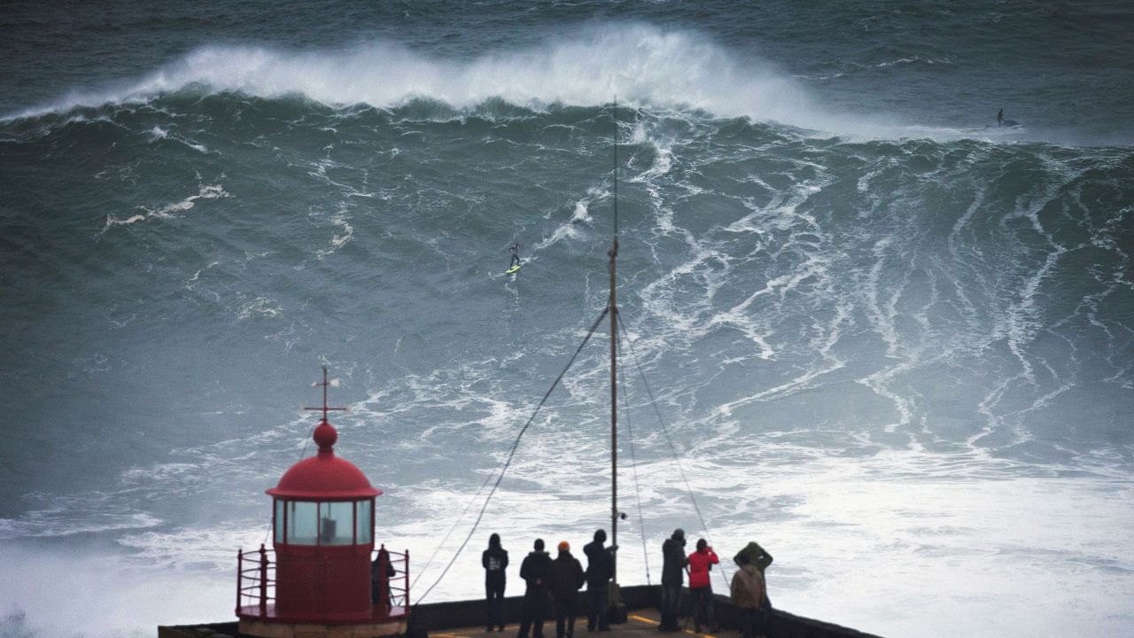 People watch a surfer ride a big wave Monday at Praia do Norte.