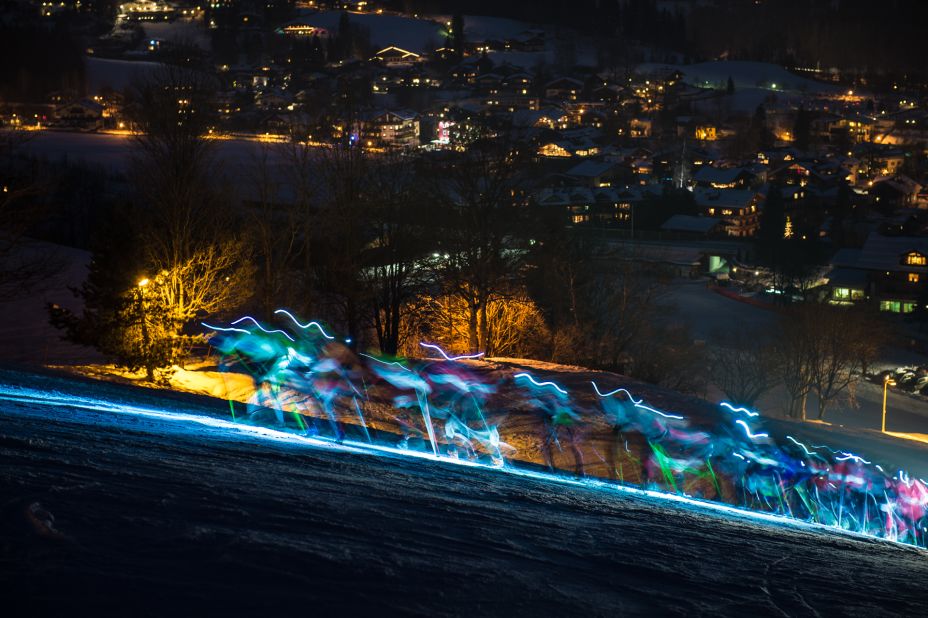 The lights of the competitors are blurred in a photographic trick as they charge up the Streif, with the Austrian resort also lit up below them. 