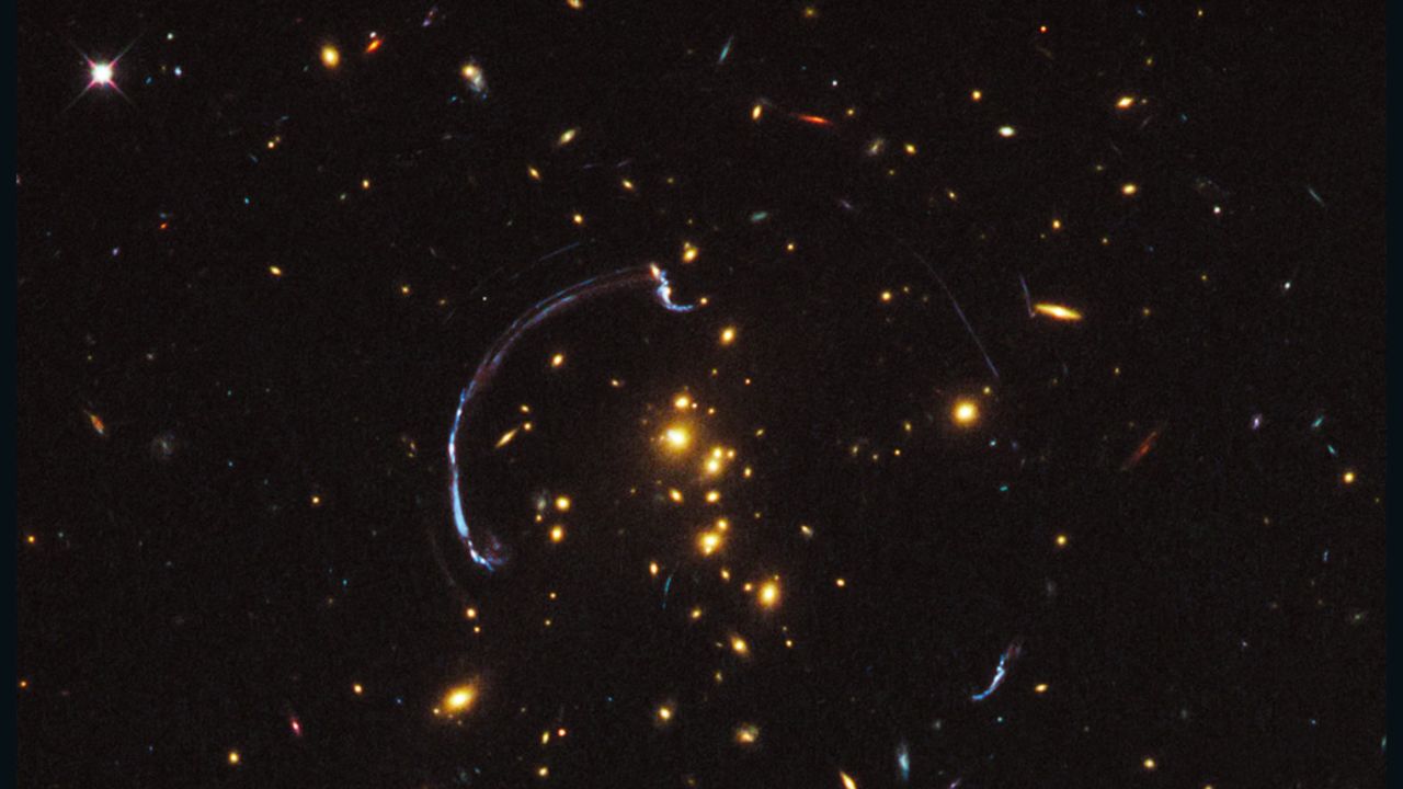 Galaxies act as a lens to stretch images of more distant galaxies, the blue arcs that are evidence of dark matter.