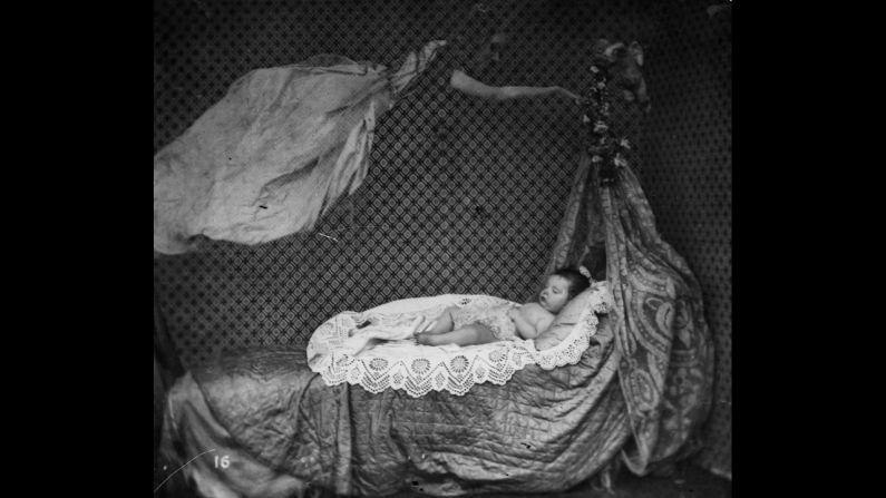 A spectral figure hovers over a sleeping baby in a crib. 