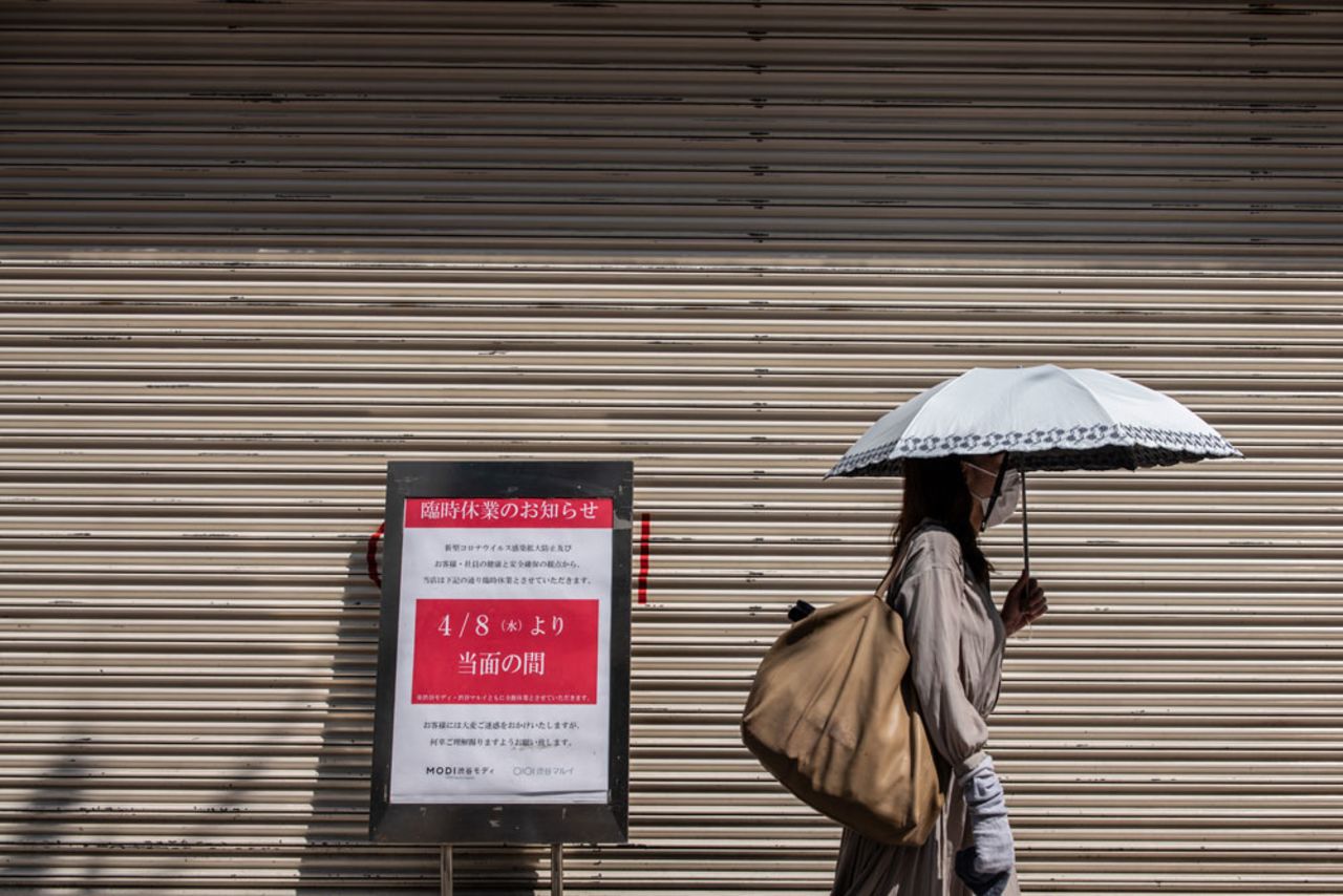 A woman holds an umbrella to shelter from the sun as she walks past a closed shop on April 8 in Tokyo, Japan.