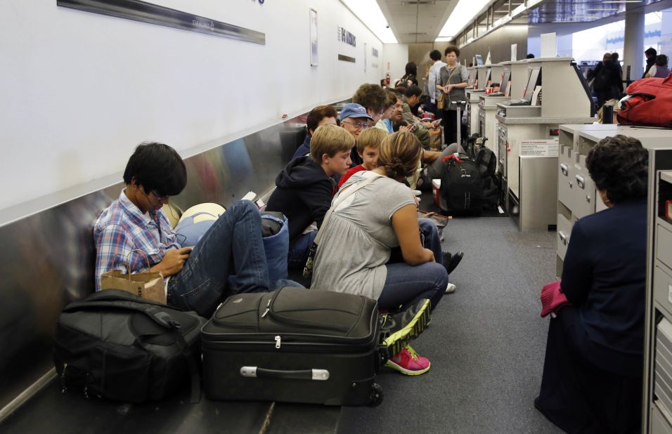Passengers sit on a luggage conveyor belt behind check-in kiosks in Terminal 1.