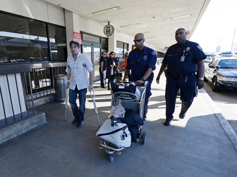 Injured traveler Bruce Reith, from Munich, Germany, is helped by two Los Angeles Airport Police officers as he makes his way on crutches to Terminal 3 for departure a day after injuring himself while escaping the shooting.