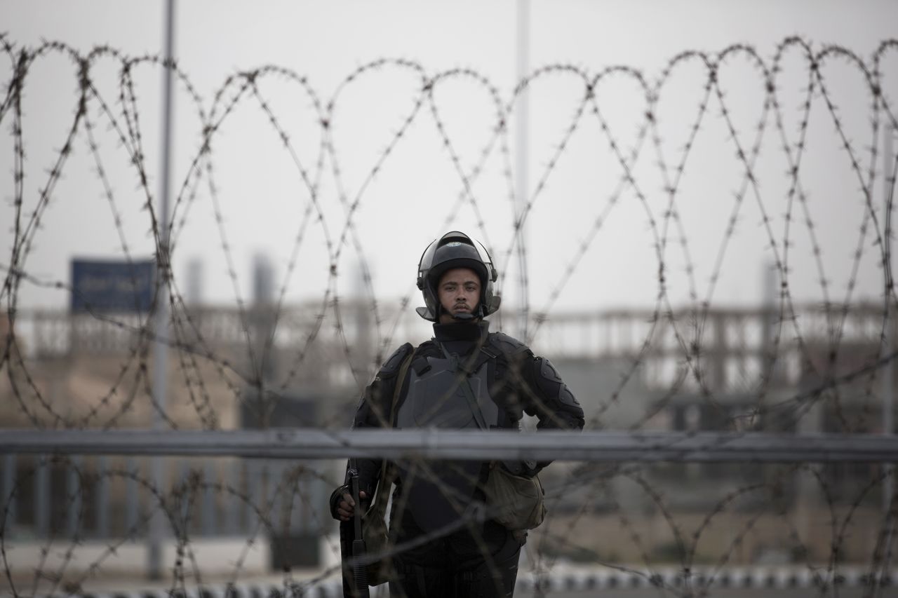 A police officer stands guard behind barbed wire.