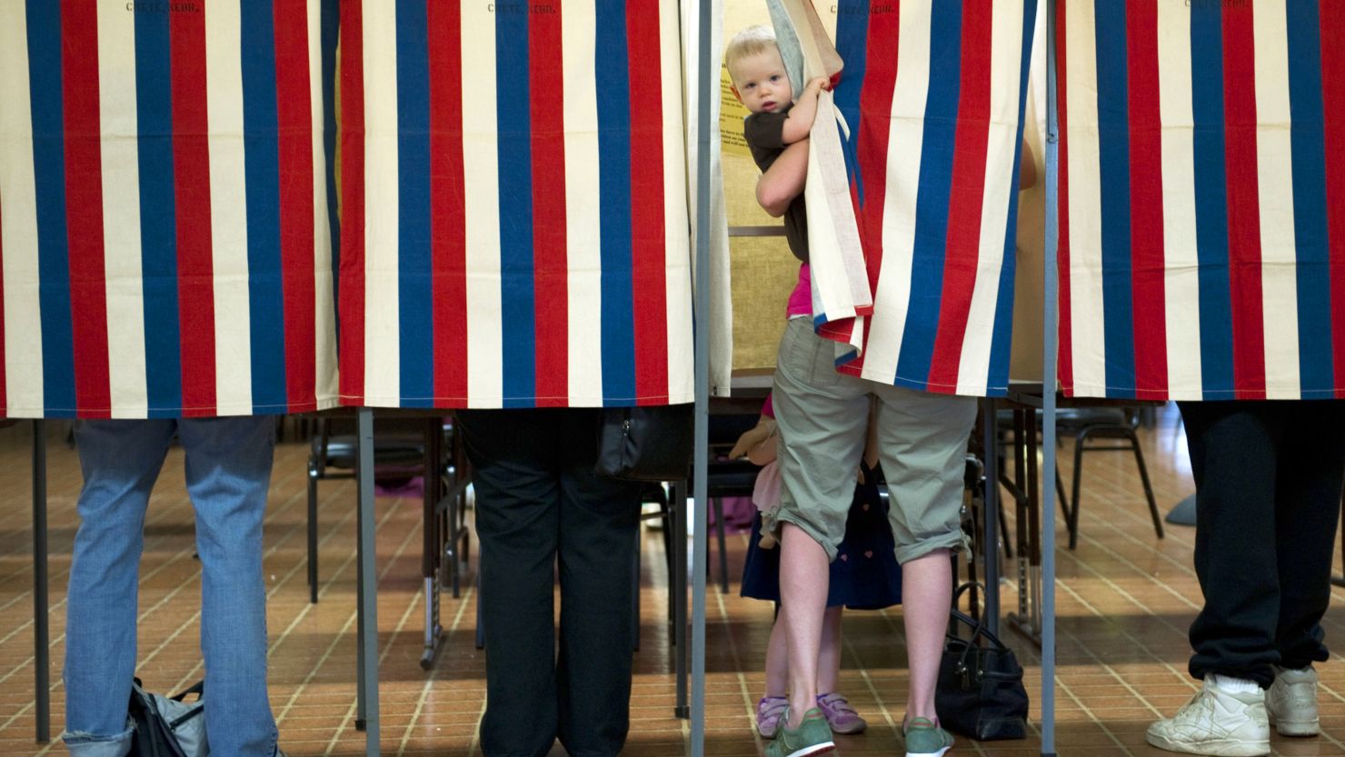 A possible future voter peeks out of the booth while his mother casts a ballot in a 2012 election in Metamora, Illinois.