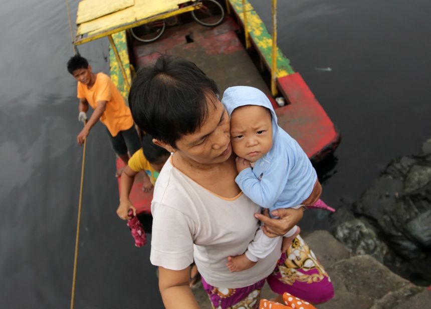 A woman carries a baby across a river November 8 at a coastal village in Las Pinas, Philippines.