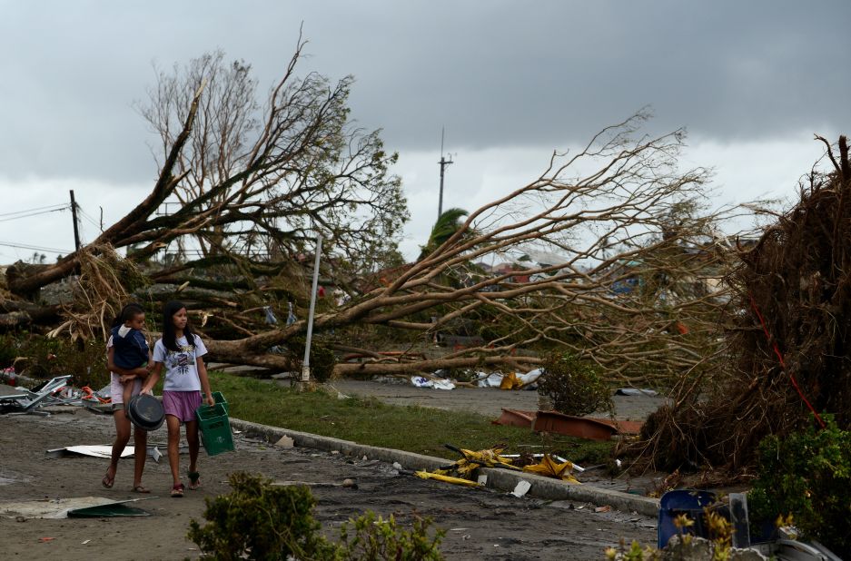 Women walk past fallen trees and destroyed houses in Tacloban on November 9. Residents scoured supermarkets for water and food as they slowly emerged on streets littered with debris.