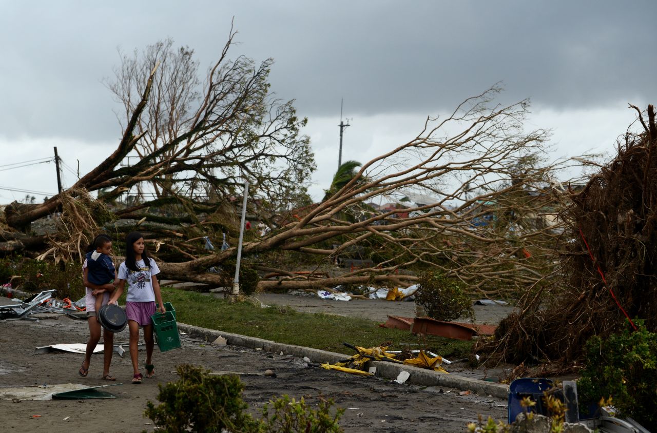 Women walk past fallen trees and destroyed houses in Tacloban on November 9. Residents scoured supermarkets for water and food as they slowly emerged on streets littered with debris.