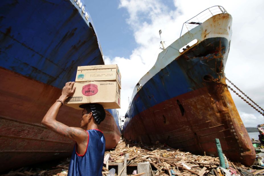 A Tacloban resident carries boxes of milk November 10 as he passes by ships washed ashore by the powerful storm.