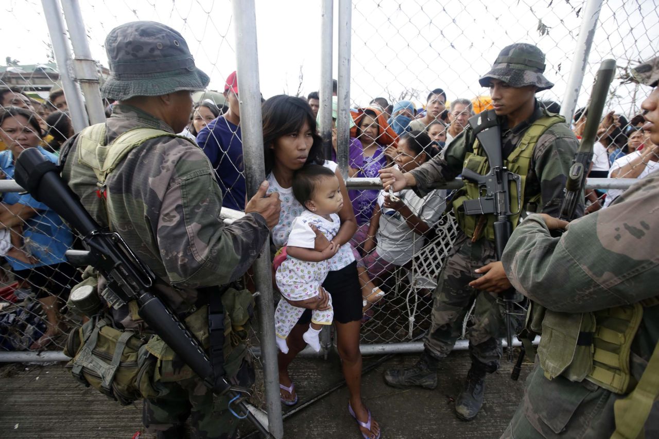 Soldados dejan entrar a una mujer y su hijo a través de una cerca para conseguir comida el 11 de noviembre a la salida del aeropuerto de Tacloban.