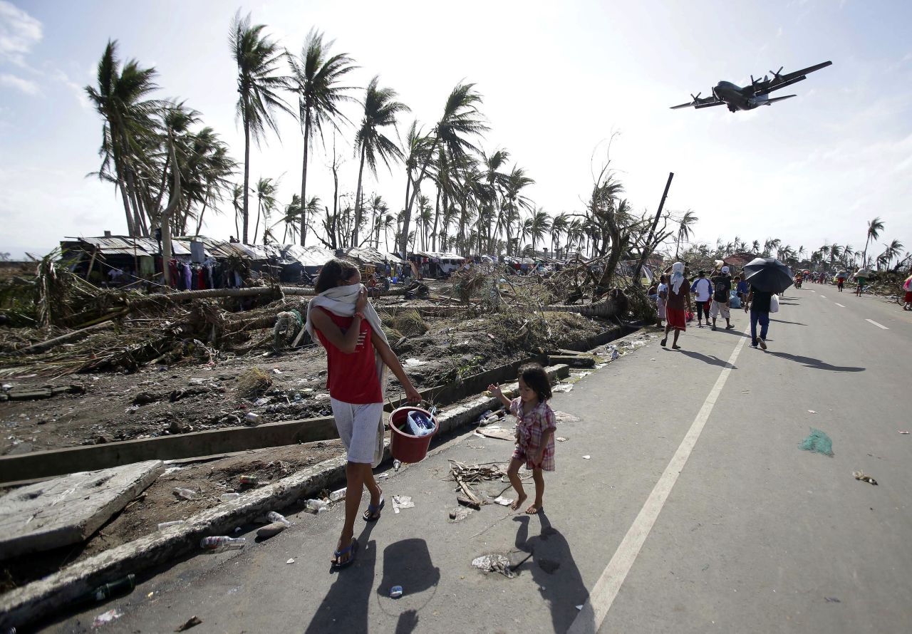 Sobrevivientes caminan por las calles de Tacloban mientras un avión militar sobrevuela por la zona devastada, el 11 de noviembre.