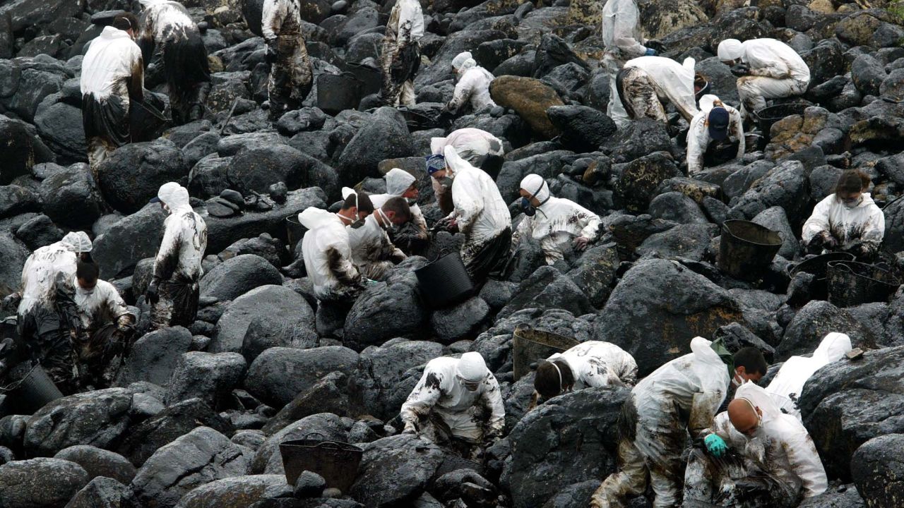 FILE PHOTO: Volunteers clean up the oil-polluted rocks of the coast in Muxia village, northwestern Spain, 17 April 2003, as efforts continue to control the environmental damage wreaked by the sunken tanker 'Prestige' which sank off Spain's northern coast in November 2002.