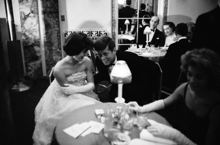 Kennedy lends an ear to his wife as they sit together at a table during cocktail hour before dining at a society gala at the Walford Astoria Hotel in 1960. 