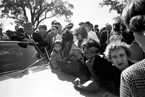 Hurchel Jacks, Vice President Johnson's driver in the motorcade, listens with others to news accounts on the car radio outside the Parkland Hospital emergency entrance. After the shots were fired, Jacks had rerouted the vice president's car to safety. The ABC radio network broadcast the first nationwide news bulletin reporting that shots have been fired at the Kennedy motorcade.