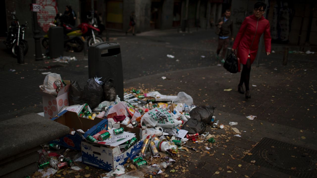 People walk past trash thrown around a trash can during the ninth day of a garbage collectors strike, in Madrid, Spain, Wednesday, Nov. 13, 2013. Street cleaners and garbage collectors who work in the city's public parks walked off the job in a strike called by trade unions to contest the planned layoff of more than 1,000 workers. Madrid's municipal cleaning companies, which have service supply contracts with the city authorities, employ some 6,000 staff. (AP Photo/Emilio Morenatti)