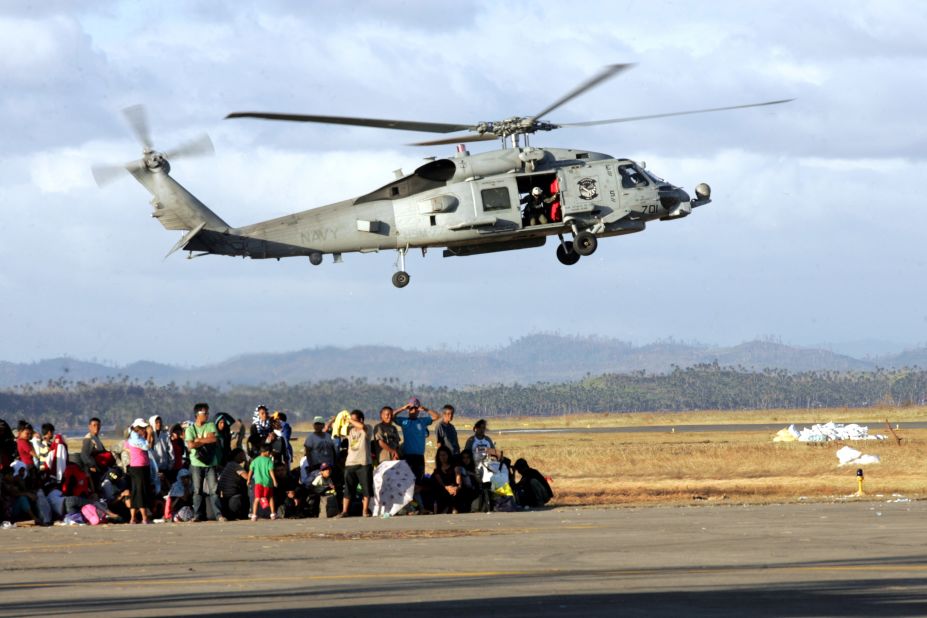 Evacuees wait to board military aircraft while a U.S. Navy helicopter takes off November 16 in Tacloban.