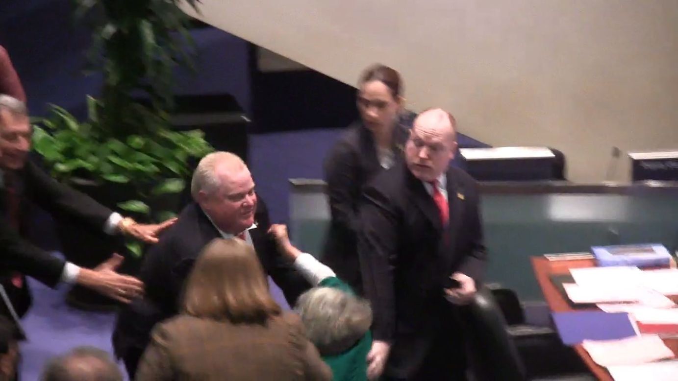 Ford accidentally knocks down Councilor Pam McConnell, in green, as he runs toward hecklers at City Hall in Toronto on Monday, November 18. That month, the city council stripped him of most of his power as mayor.