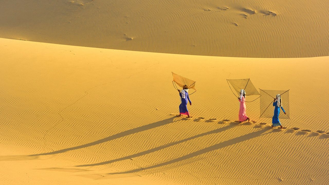 A group of Vietnamese women cross the sand dunes to the beach to go fishing.