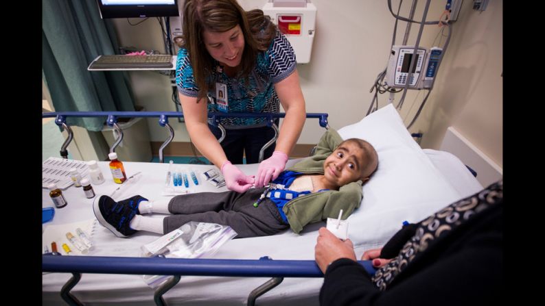 A young patient smiles at his mother while a nurse prepares him for treatment.