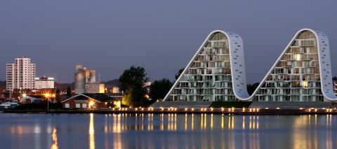 The Wave building in the Danish town of Vejle mirrors the soft movements on the surface of the fjord during the day and resembles illuminated mountain peaks at night. 