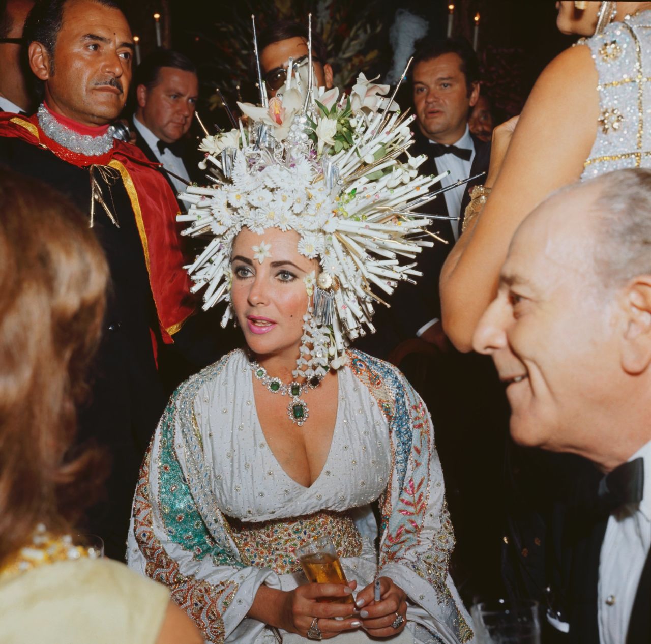 Elizabeth Taylor was famous for wearing flamboyant jewelry, and her collection featured some extremely valuable pieces. Here she is wearing an elaborate headdress of pearls and fake flowers, but her emerald necklace still stands out.