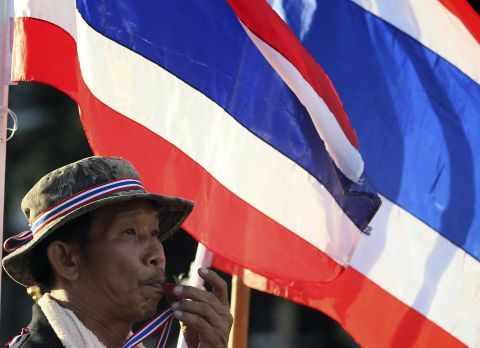An anti-government protester blows a whistle in front of Thai flags during a rally at Bangkok's Democracy Monument on Friday, one day after the embattled Prime Minister Yingluck Shinawatra survived a no-confidence vote in parliament.