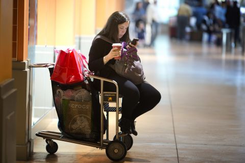A woman sits on a shopping cart at Miami's Dolphin Mall as she checks prices on her smartphone on November 29. 
