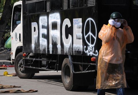 An anti-government protester walks past a police vehicle with the word "peace" painted where "police" used to be.