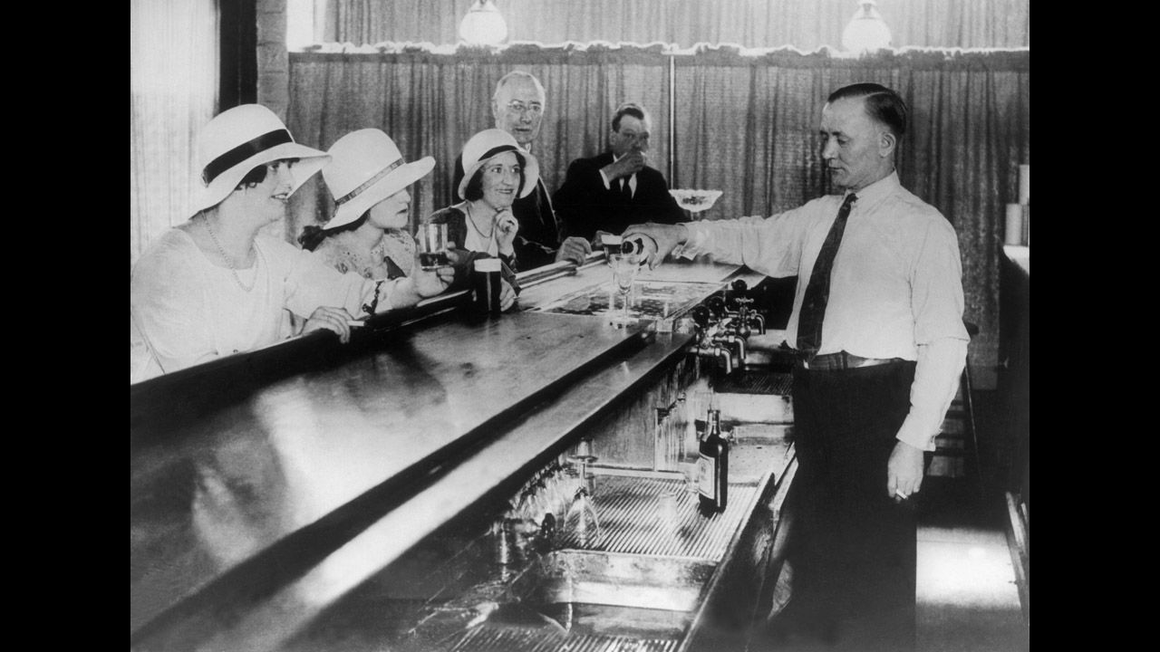 Men and women inside a New York speakeasy in 1930. These illegal bars, developed during Prohibition. They were sometimes frequented by a chic clientele looking to consume alcohol. Speakeasies got their name for the need to whisper or "speak easy," and a secret knock or password could be required for a person to enter the establishment. 