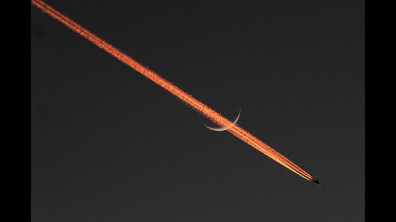 <strong>December 5:</strong> An airplane passes the moon, leaving behind a vapor trail over Lahore, Pakistan.