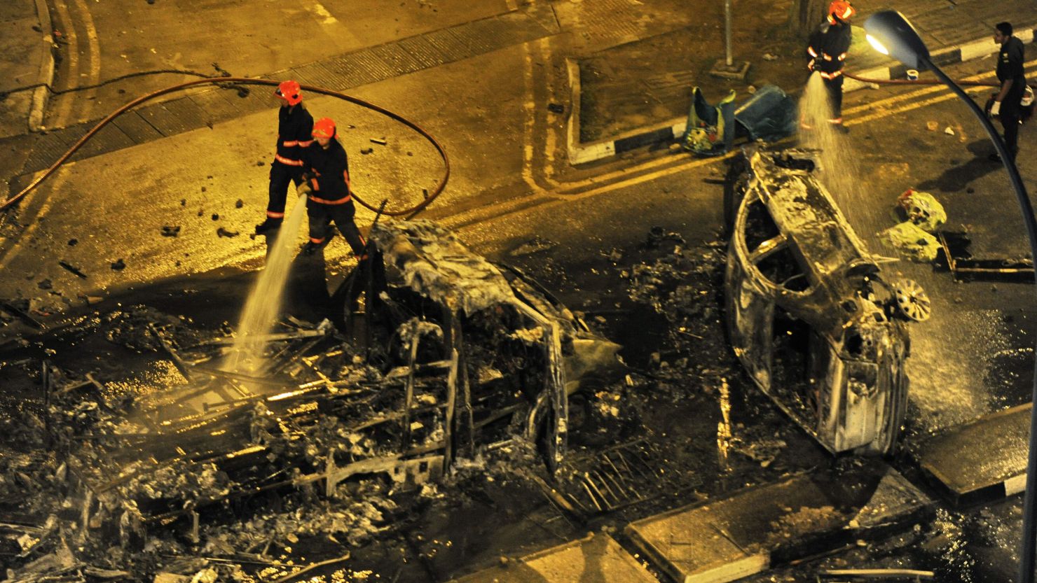 Firemen douse a charred ambulance and a car in the early hours of Monday, after a riot broke out among South Asian workers in Singapore.