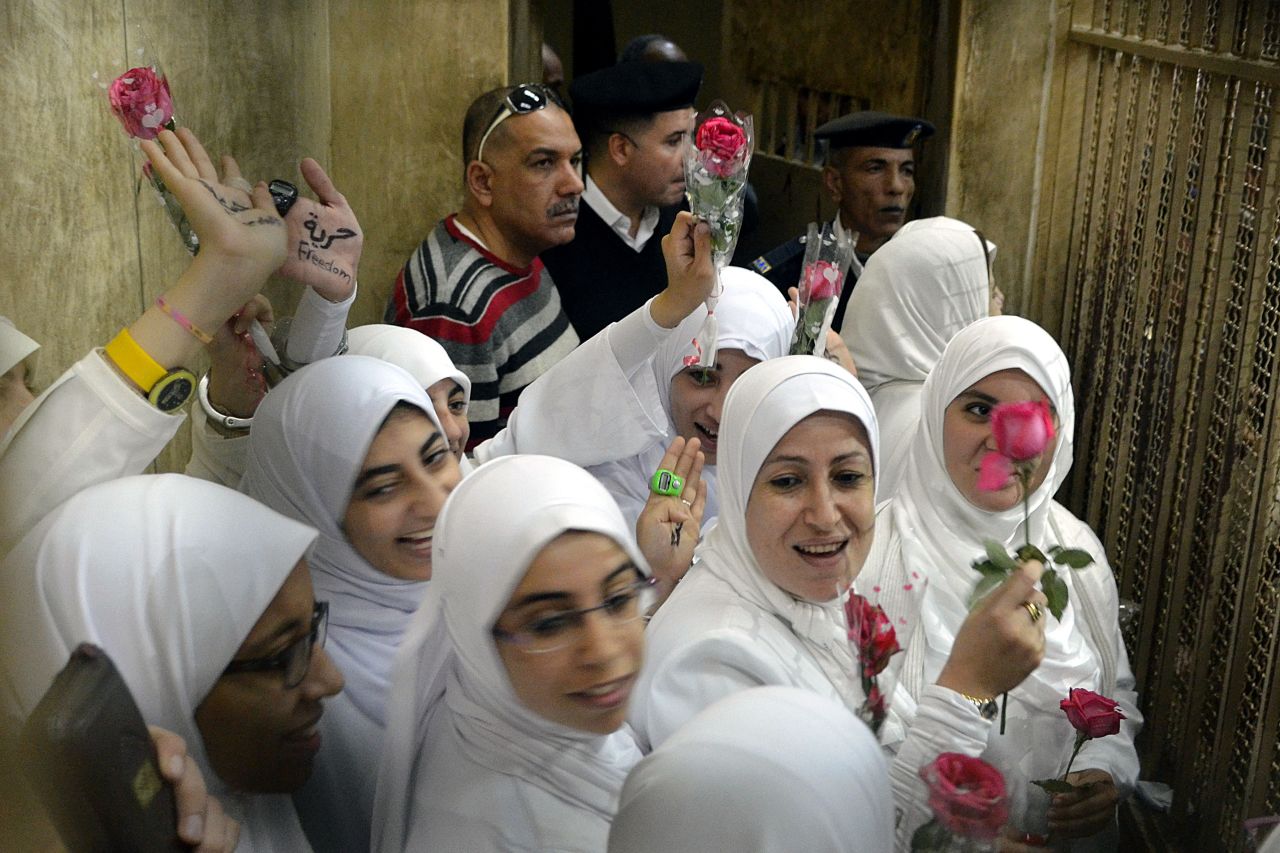 Egyptian women members of the Muslim Brotherhood hold roses as they stand in the defendants' cage dressed in prison issue white during their trial in at the court in the Egyptian Mediterranean city of Alexandria on December 7, 2013. 