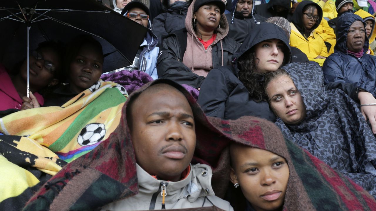 People take shelter under blankets and umbrellas during the memorial service.