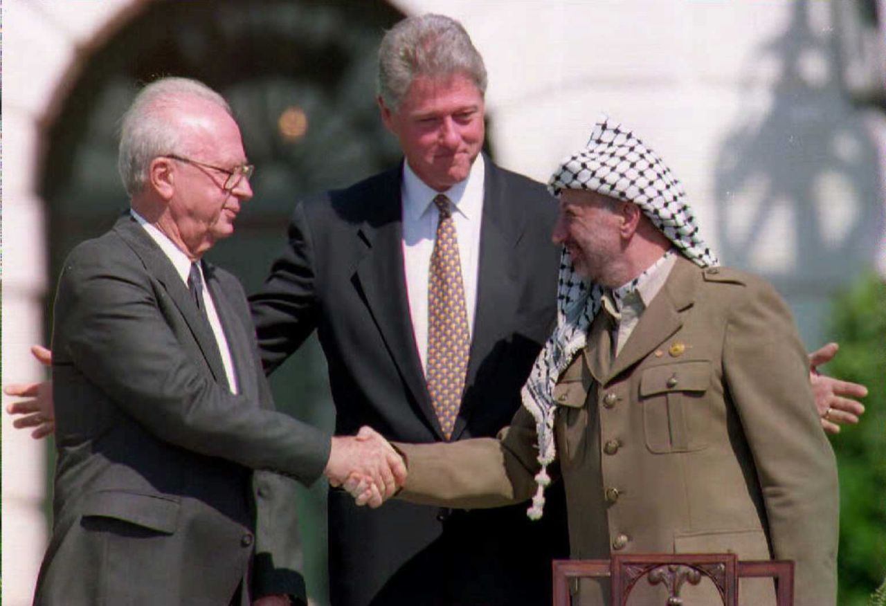 U.S. President Bill Clinton stands behind PLO leader Yasser Arafat, right, and Israeli Prime Minister Yitzahk Rabin as the two shake hands on October 25, 1995. Rabin and Arafat shook hands for the first time after Israel and the PLO signed a historic agreement on Palestinian autonomy in the occupied territories.