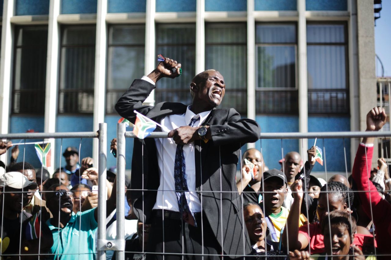 A cheering man climbs up a fence after the casket of Mandela passed on its way to the Union Buildings on December 13.