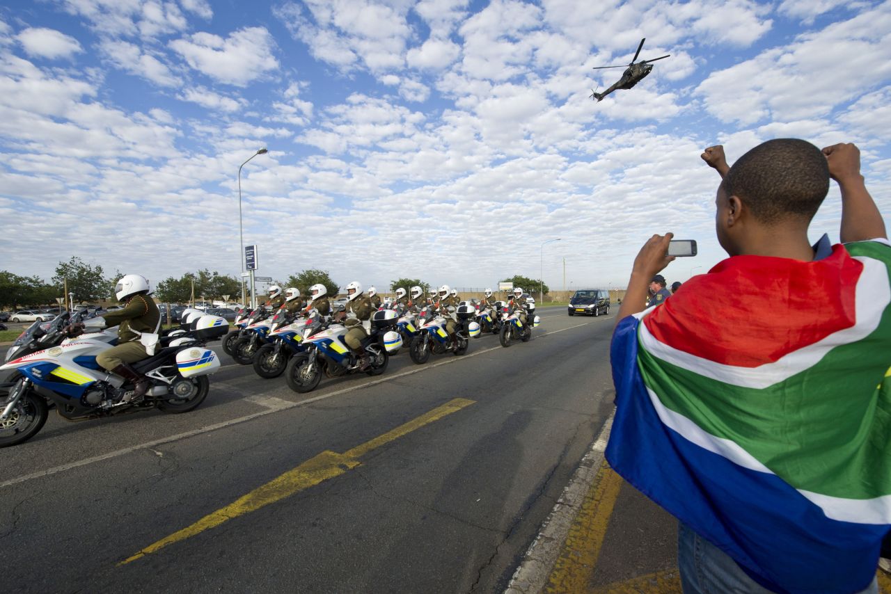 A child draped in the South African flag takes a photo of the procession as the body of Mandela arrives at the Waterkloof air base.