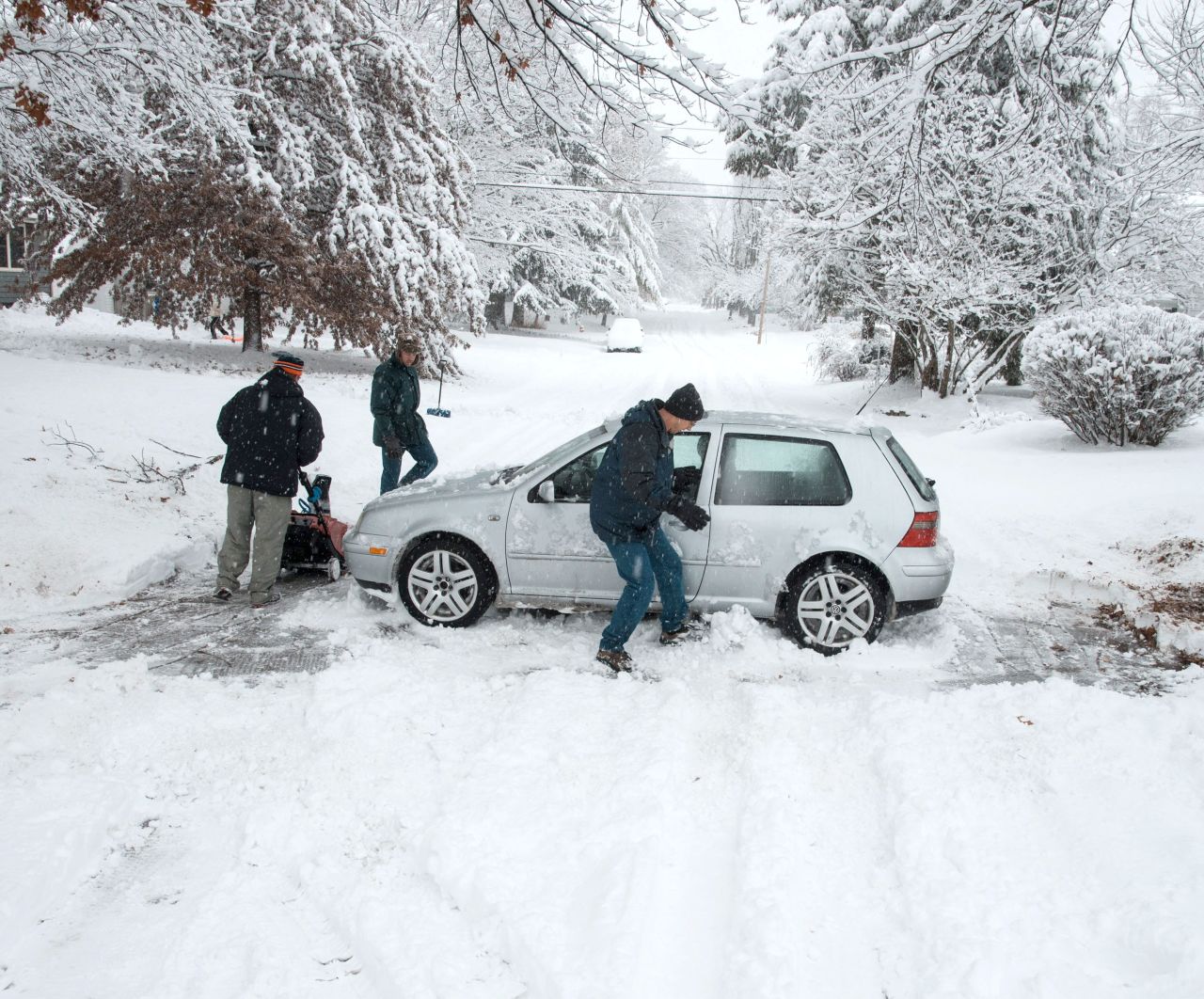 Dave Andsager, right, kicks snow out from under his car on in Champaign, Illinois, as neighbors Andy Dixon, left, and Dave Mattson help him dig out on December 14.