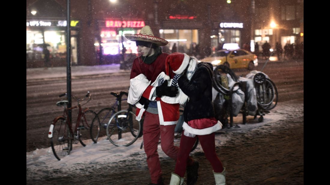 Snow falls on a couple of chilly Santas as they make their way through Manhattan. 