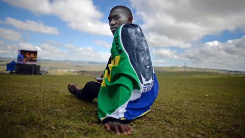 A man sits on a hill as the ceremony is broadcast on huge screens at Mandela's burial site in Qunu.
