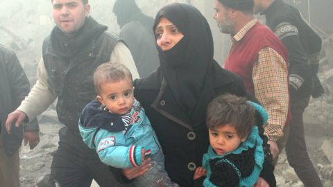 A Syrian woman carries children following airstrikes on a rebel area of the war-torn city of Aleppo on December 15, 2013. 