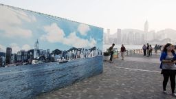 A tourist walks past a billboard featuring a backdrop of the city skyline with a clear sky on October 25 in Hong Kong.