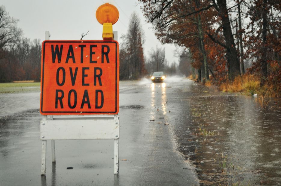 A sign warns drivers of a flooded road while a car charges through heavy rainfall on Saturday, December 21 in Paducah, Kentucky.