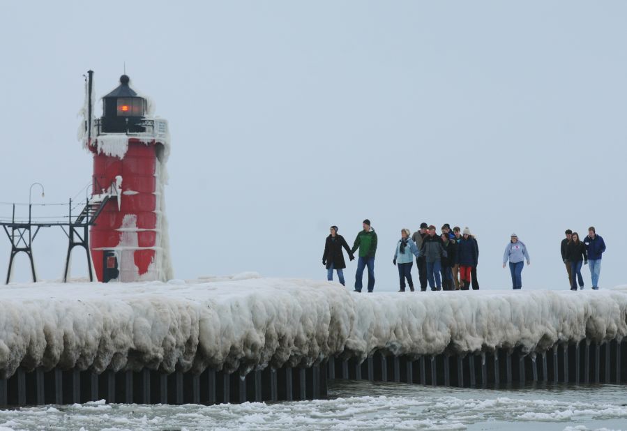 People walk along an ice-covered pier near the South Haven Lighthouse on December 21 in South Haven, Michigan.