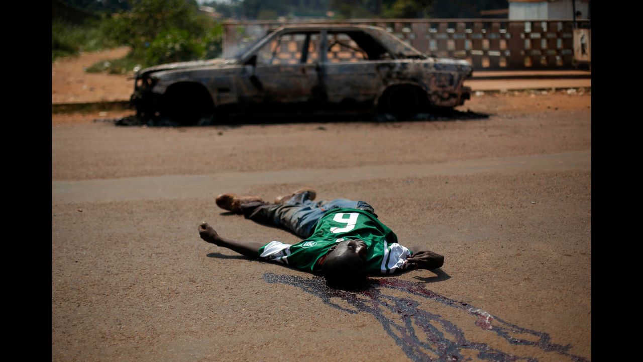 The body of a suspected militiaman lies in the road near a charred car in Bangui on Friday, December 20.