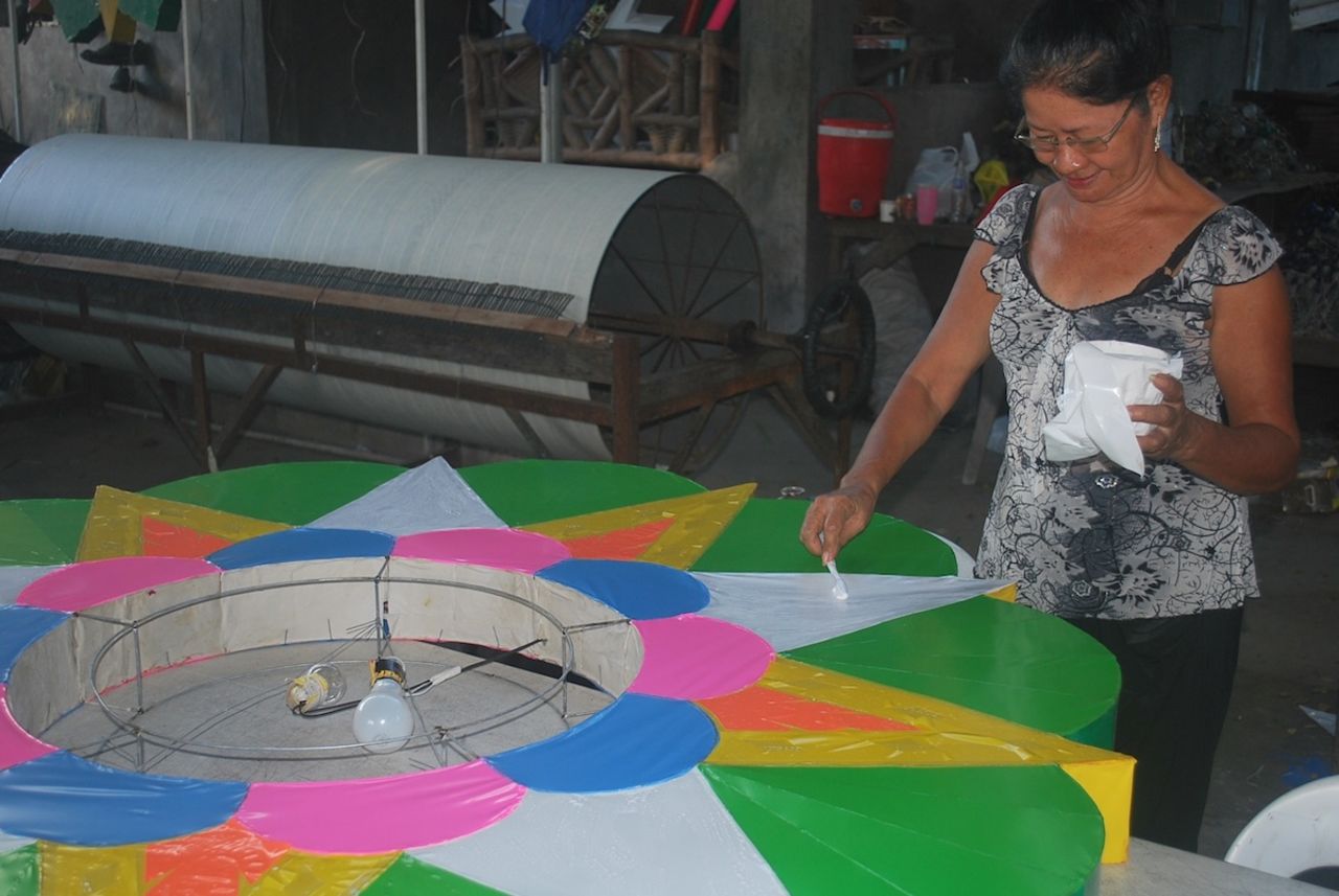An employee in Quiwa's workshop puts the finishing touches on a small parol ordered by a school in Manila. In the background is an unfinished 'rotor,' a steel drum that serves as the light switch on a giant parol. 