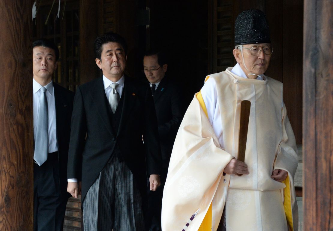 A Shinto priest (R) leads Japanese Prime Minister Shinzo Abe (C) as he visits the controversial Yasukuni war shrine in Tokyo on December 26, 2013.